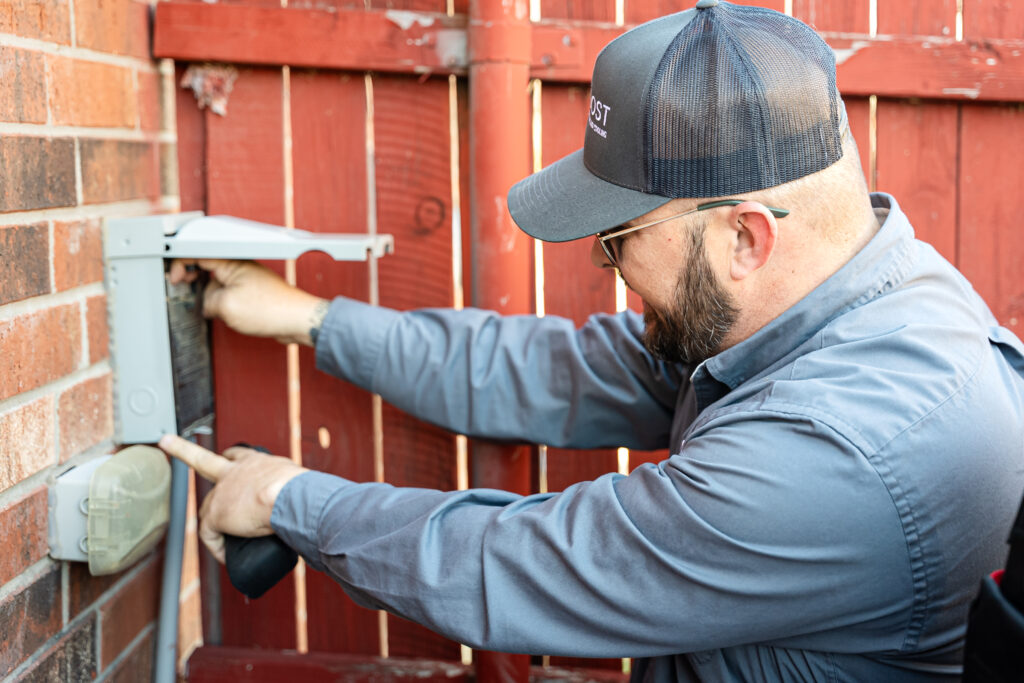 Electrician servicing outdoor disconnect box on brick wall for Boost Air HVAC